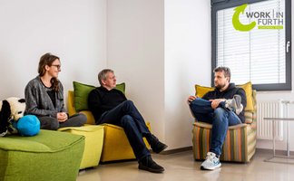 Drei Personen sitzen auf bequemen Sofas und unterhalten sich in einer modernen, entspannten Arbeitsumgebung