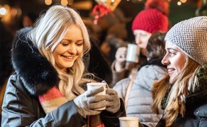 Zwei Frauen halten Tassen Glühwein auf der Altstadtweihnacht, umgeben von festlicher Beleuchtung.