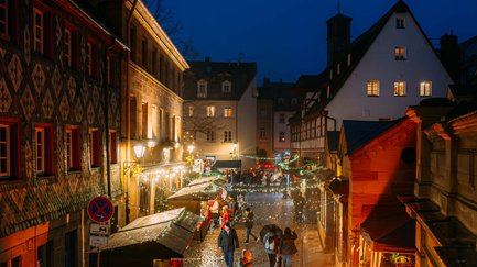 Besucher schlendern durch die festlich beleuchtete Waagstraße mit Buden, Feuerschale und Lichterkette.