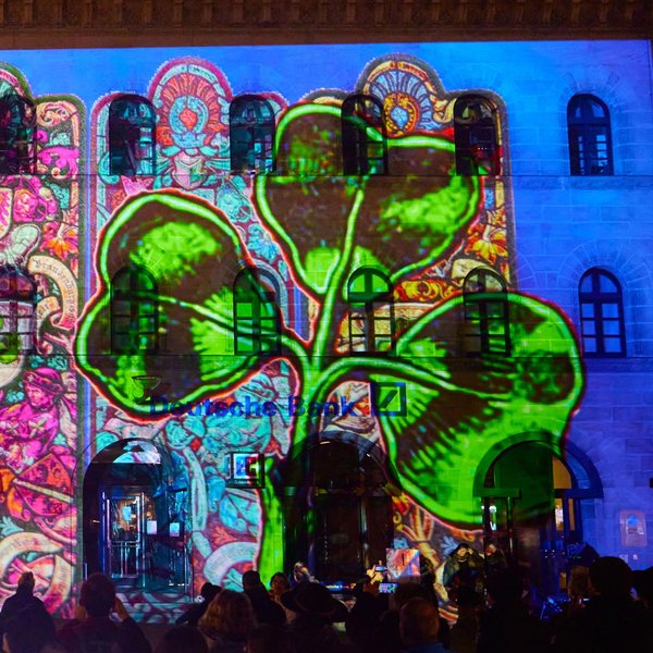 Lichtprojektionen der Glanzlichter Fürth auf historischem Gebäude, umgeben von Besuchern bei Nacht.