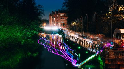 Uferpromenade in Fürth bei Nacht, farbig beleuchtet mit Reflexionen auf der Wasseroberfläche.