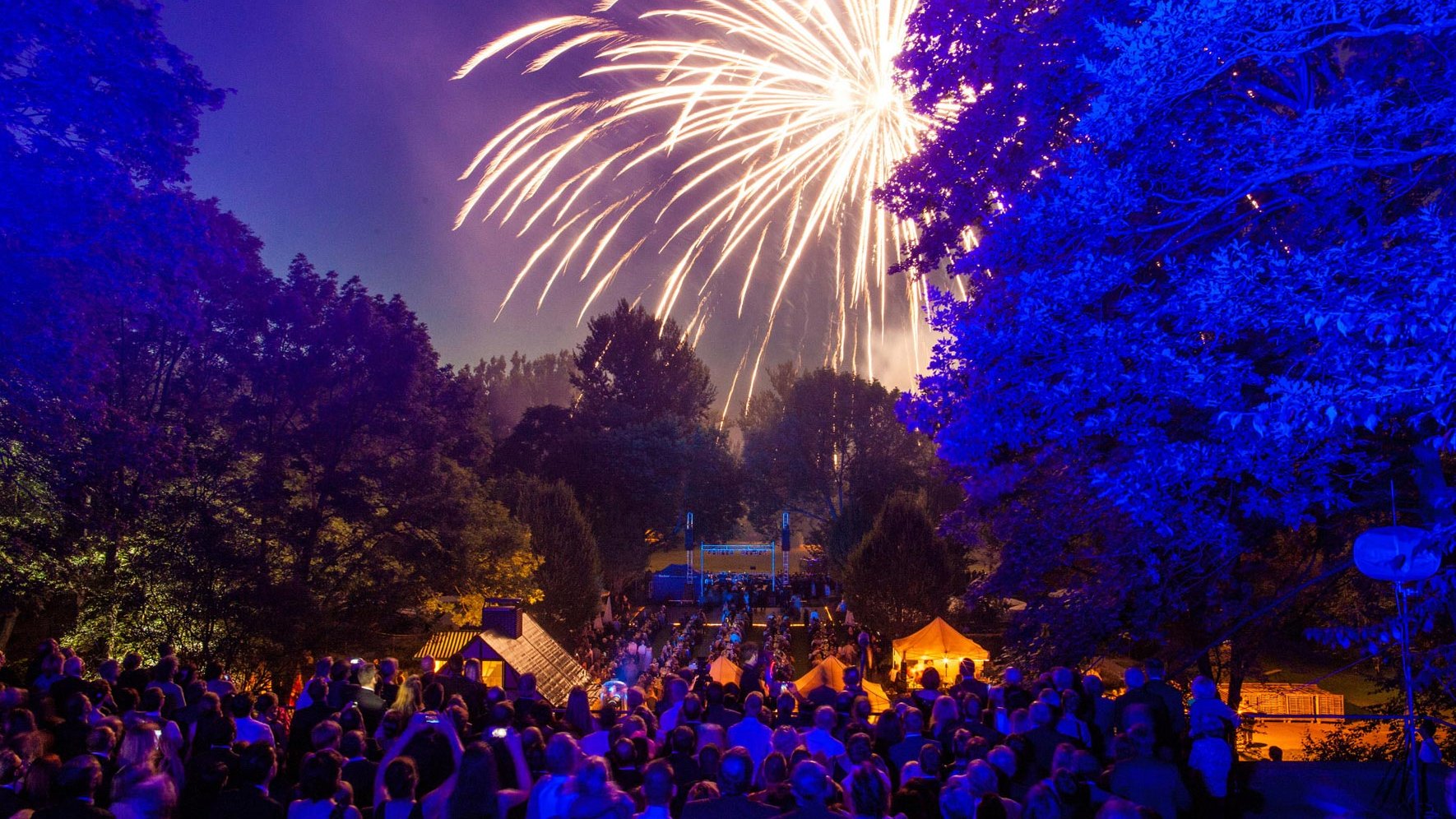 Besucher feiern unter freiem Himmel beim Sommernachtsball und bewundern das Feuerwerk