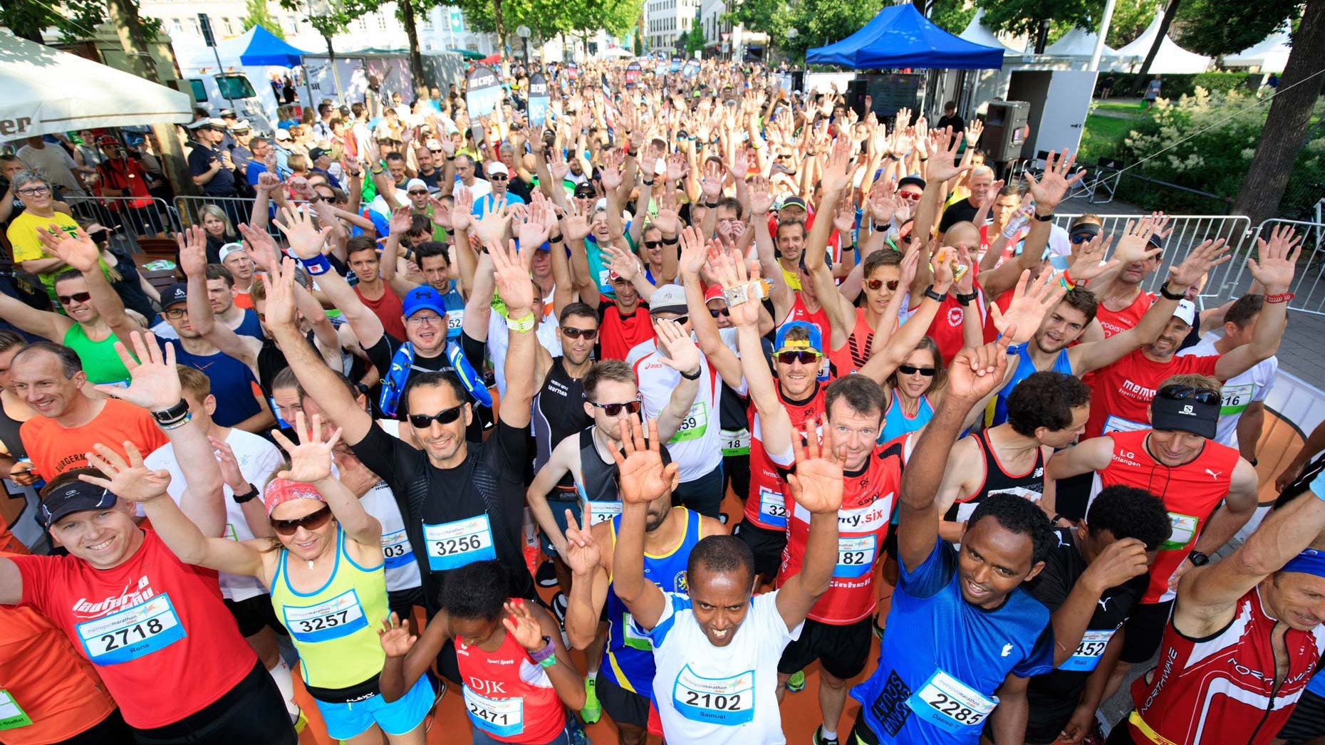 Teilnehmer des Sparkassen Metropolmarathons in Sportkleidung mit Nummern heben die Hände freudig