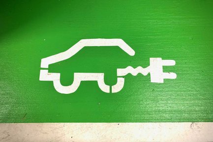 Grüne Wand mit weißem E-Auto-Symbol und Ladestecker markiert Elektro-Ladeplatz für Fahrzeuge