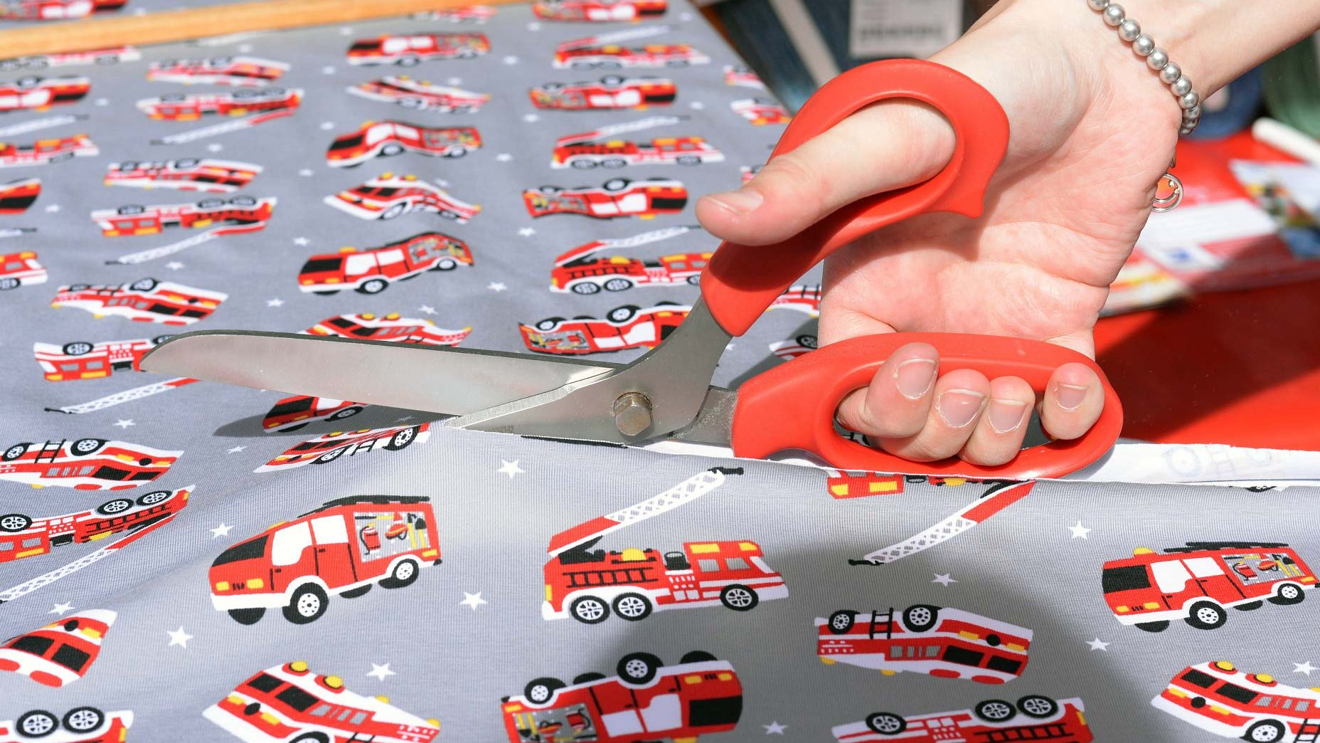 Nahaufnahme von Kinderstoff mit Feuerwehrautos, der auf dem Stoffmarkt zugeschnitten wird.