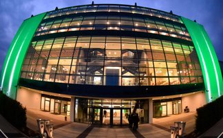 Modernes Außengebäude der Haupttribüne im Sportpark Ronhof | Thomas Sommer, grün beleuchtet mit großer Glasfassade