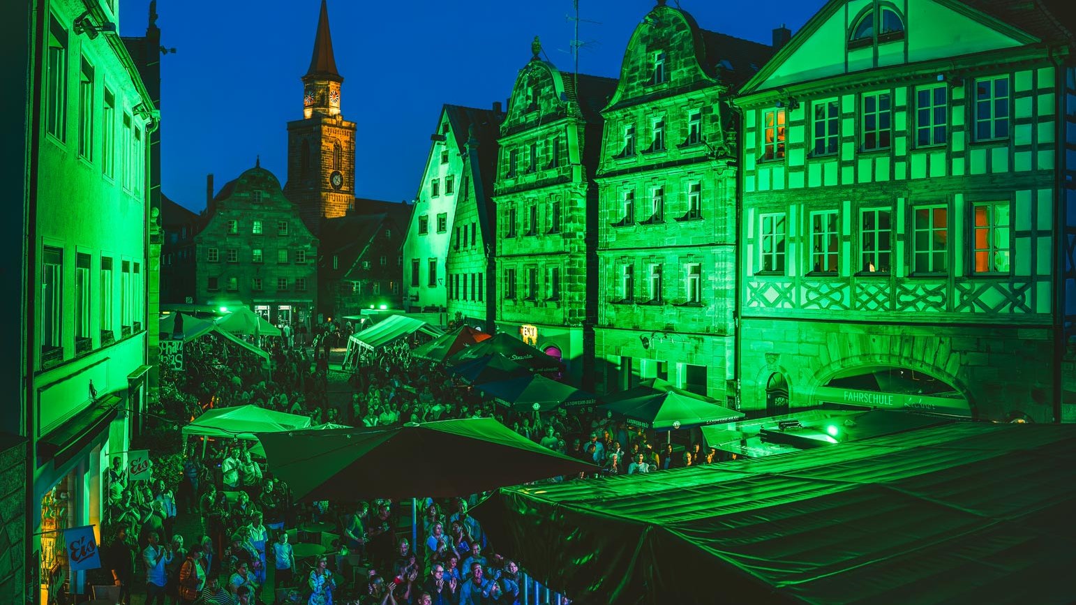 Menschen tanzen auf dem Grünen Markt, grün beleuchtete Gebäude und Livemusik auf Bühne