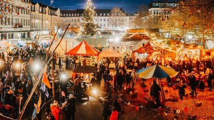 Menschen schlendern über den Mittelalter- und Weihnachtsmarkt auf der Fürther Freiheit mit warmen Lichtern.