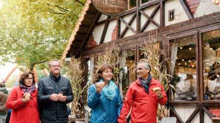 Zwei Paare mit Bratwurstsemmeln vor temporären Wirtshäusern auf der Michaelis-Kirchweih.