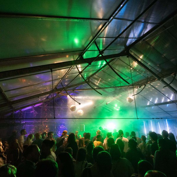 Tanzende Gäste im festlich beleuchteten Gewächshaus mit DJ, Lichtern und Discokugeln beim Festgartenfest.