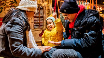 Familie in Gondel des Kinderkarussells auf hell erleuchtetem Weihnachtsmarkt.