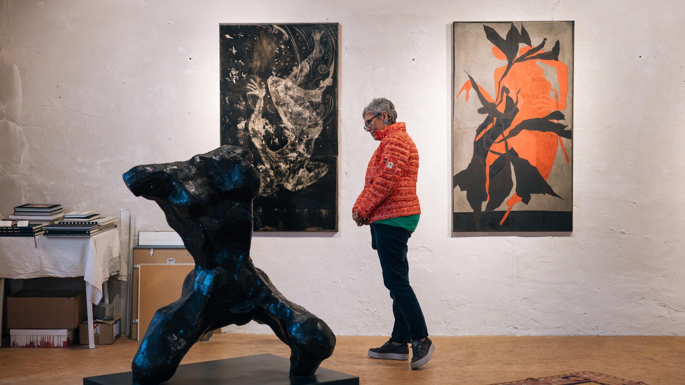Person betrachtet schwarze Skulptur in heller Galerie mit abstrakter Kunst an den Wänden.