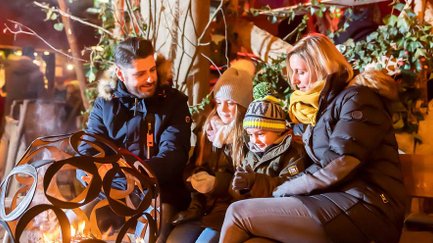 Familie sitzt in Winterkleidung am Feuer einer Feuerschale auf dem Fürther Mittelaltermarkt vor den Ständen.