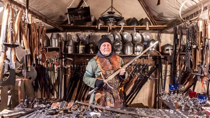Händler in mittelalterlicher Kleidung präsentiert Schwerter, Äxte und Helme auf Fürther Mittelaltermarkt.