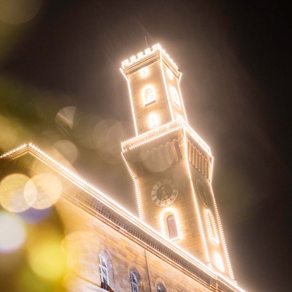 Das Rathaus mit Turm ist nachts in warmem LED-Licht zum Weihnachtsmarkt stimmungsvoll beleuchtet.