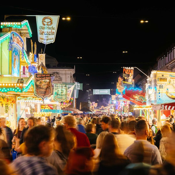 Menschen schlendern am Abend zwischen bunt beleuchteten Buden der Michaelis-Kirchweih entlang.