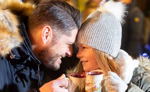 Vater und Tochter sitzen eng beisammen, lachen sich an und stoßen mit ihren Weihnachtstassen an.