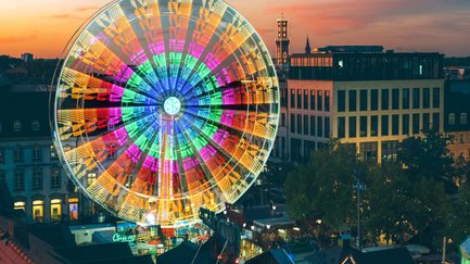 Das Riesenrad auf der Fürther Freiheit zur Michaelis-Kirchweih dreht sich bunt beleuchtet bei Abenddämmerung.