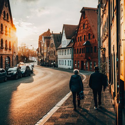 Älteres Paar spaziert im Abendlicht an Sandstein- und Fachwerkhäusern durch die Fürther Altstadt