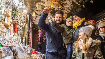 Familie betrachtet eine Christbaumkugel an einem festlich geschmückten Stand auf dem Weihnachtsmarkt.
