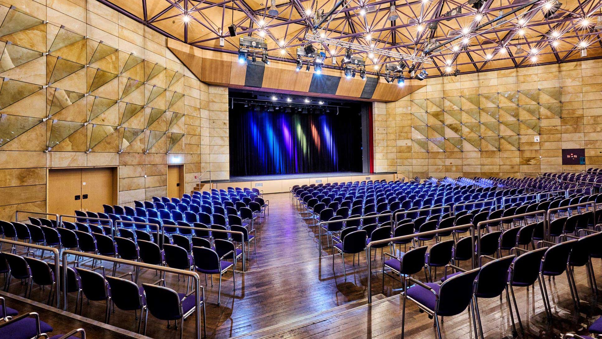 Großer heller Saal der Stadthalle mit Stuhlreihen, Bühne, Holzverkleidung und Deckenbeleuchtung.