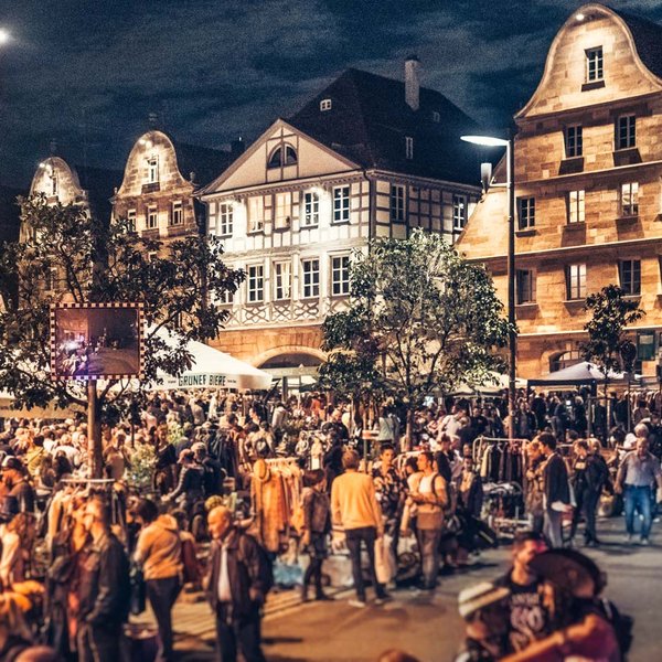 Nachtaufnahme des Graffelmarkts mit Altstadthäusern und lebendigen Flohmarktständen.