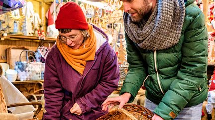 Paar in Winterkleidung betrachtet handgeflochtene Körbe und Weihnachtsdekoration an einem Stand.